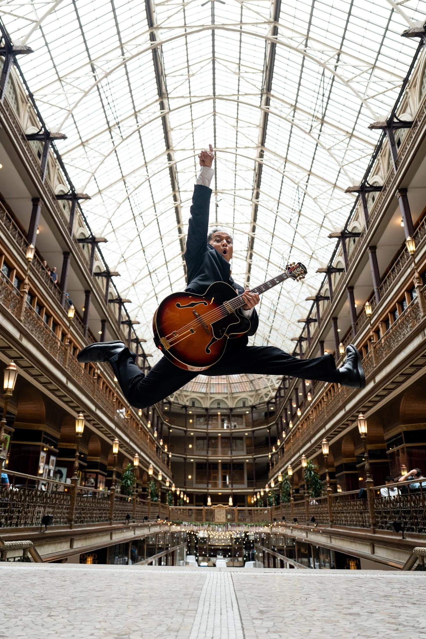 Gary Dacanay leaping with a sunburst hollow-body guitar beneath an ornate glass ceiling.